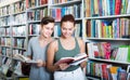 Two positive teenagers reading book together in shop Royalty Free Stock Photo