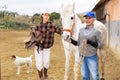 Two positive women preparing horse for riding in paddock Royalty Free Stock Photo