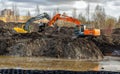Two powerful excavators in the park dig a pond pouring earth from a bucket