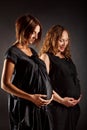 Two pregnant women in black dresses touching their belly and thinking about future