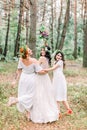 Two pretty bridesmaids surround bride with backs turned, full length portrait on forest background. Women in white