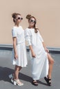 Two pretty cute fashion girl girlfriends in white gowns posing for fashion clothing catalog in sunglasses on a bright sunny summer Royalty Free Stock Photo