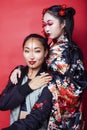 Two pretty geisha girls friends: modern asian woman and traditional wearing kimono posing cheerful on red background Royalty Free Stock Photo