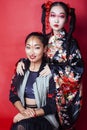 Two pretty geisha girls friends: modern asian woman and traditional wearing kimono posing cheerful on red background Royalty Free Stock Photo