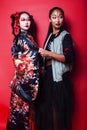 Two pretty geisha girls friends: modern asian woman and traditional wearing kimono posing cheerful on red background Royalty Free Stock Photo