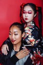 Two pretty geisha girls friends: modern asian woman and traditional wearing kimono posing cheerful on red background Royalty Free Stock Photo