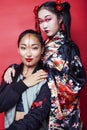 Two pretty geisha girls friends: modern asian woman and traditional wearing kimono posing cheerful on red background Royalty Free Stock Photo