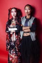 Two pretty geisha girls friends: modern asian woman and traditional wearing kimono posing cheerful on red background Royalty Free Stock Photo