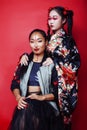 Two pretty geisha girls friends: modern asian woman and traditional wearing kimono posing cheerful on red background Royalty Free Stock Photo