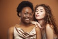 Two pretty girls african and caucasian blond posing cheerful together on browm background, etnithity diverse lifestyle Royalty Free Stock Photo