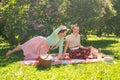 Two pretty girls friends sitting on the red blanket on the green grass and have summer picnic. happy woman having rest and fun on