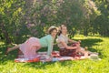 Two pretty girls friends sitting on the red blanket on the green grass and have summer picnic. happy woman having rest and fun on