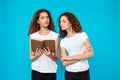 Two pretty girls twins reading book over blue background.