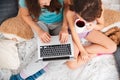 Two pretty happy sisters drinking tea and using laptop together