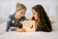 Two pretty little girls sisters, lying on bed at home and enjoying their time playing with wooden night lamp with moon Royalty Free Stock Photo