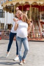 Two pretty women in amusement park having fun and eating sweets, happy family. Samesex lesbian family, pregnant couple.
