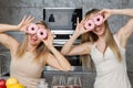 Two pretty women have made themselves glasses out of doughnuts and are having fun in the kitchen.