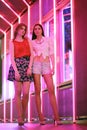 Two pretty women pose near pink illuminated wall