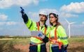 Two professional maintenance engineers in uniform and safety workwear using tablet to checklist repair wind turbines on windmill
