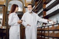 Two professional pharmacists, senior bearded man and young woman, working at ancient pharmacy. Male pharmacist holding