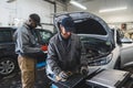 two professional servicemen making car diagnostics on a laptop and smiling, medium shot car repair shop Royalty Free Stock Photo