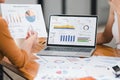 Two professionals analyze business data using laptop displaying sales dashboard and various printed charts on desk. Royalty Free Stock Photo