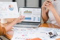 Two professionals analyze business data using laptop displaying sales dashboard and various printed charts on desk. Royalty Free Stock Photo