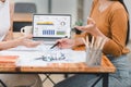 Two professionals analyze business data using laptop displaying sales dashboard and various printed charts on desk. Royalty Free Stock Photo