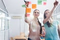 Two proficient female co-workers posting sticky notes in the int