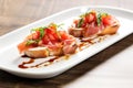 two prosciutto bruschetta pieces on a rectangular white plate