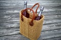 Heading to a garden party - Two wine or champagne bottles in woven straw tote bag, sitting on weathered wooden deck