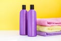 Two purple cosmetic bottles and three towels on a lilac background Royalty Free Stock Photo