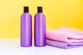 Two purple cosmetic bottles and two towels on a lilac background Royalty Free Stock Photo