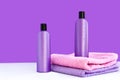 Two purple cosmetic bottles on two towels on a lilac background. Spa concept Royalty Free Stock Photo