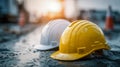 Two rain-soaked protective helmets in yellow and white resting on a wet surface at a construction site under a soft glowing sunset Royalty Free Stock Photo