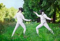 Two rapier fencer women fighting over beautiful nature