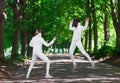 Two rapier fencer women fighting over park alley