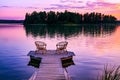 Two rattan chairs and glasses of red wine on a pier overlooking a lake at sunset in Finland Royalty Free Stock Photo