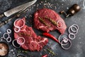 Two Raw beef steak with spices, onions and chili on dark slate or concrete background. Royalty Free Stock Photo