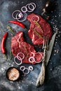 Two Raw beef steak with spices, onions and chili on dark slate or concrete background. Royalty Free Stock Photo