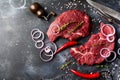 Two Raw beef steak with spices, onions and chili on dark slate or concrete background. Royalty Free Stock Photo