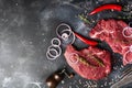 Two Raw beef steak with spices, onions and chili on dark slate or concrete background. Royalty Free Stock Photo