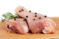 two raw chicken drumsticks on a wooden cutting boardn with a sprig of dill and peppercorns white background