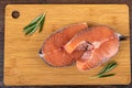 Two raw fresh portioned salmon steaks and rosemary sprigs on a cutting board.