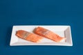 Two raw salmon loins seasoned with salt and pepper on a rectangular white ceramic platter on a blue studio background. Royalty Free Stock Photo