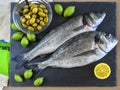 Two ready to cook raw fish with lemon and olives on stone slate Royalty Free Stock Photo