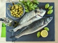 Two ready to cook raw fish with lemon and olives on stone slate Royalty Free Stock Photo