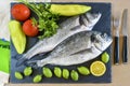 Two ready to cook raw fish with lemon and tomatoes on stone slat Royalty Free Stock Photo