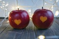 Two red apples with a heart seal on the table. Orange heart on organically grown fruits. Growing fruits with prints.