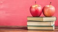 Two red apples sitting atop a stack of three books against a textured pink background surface Royalty Free Stock Photo